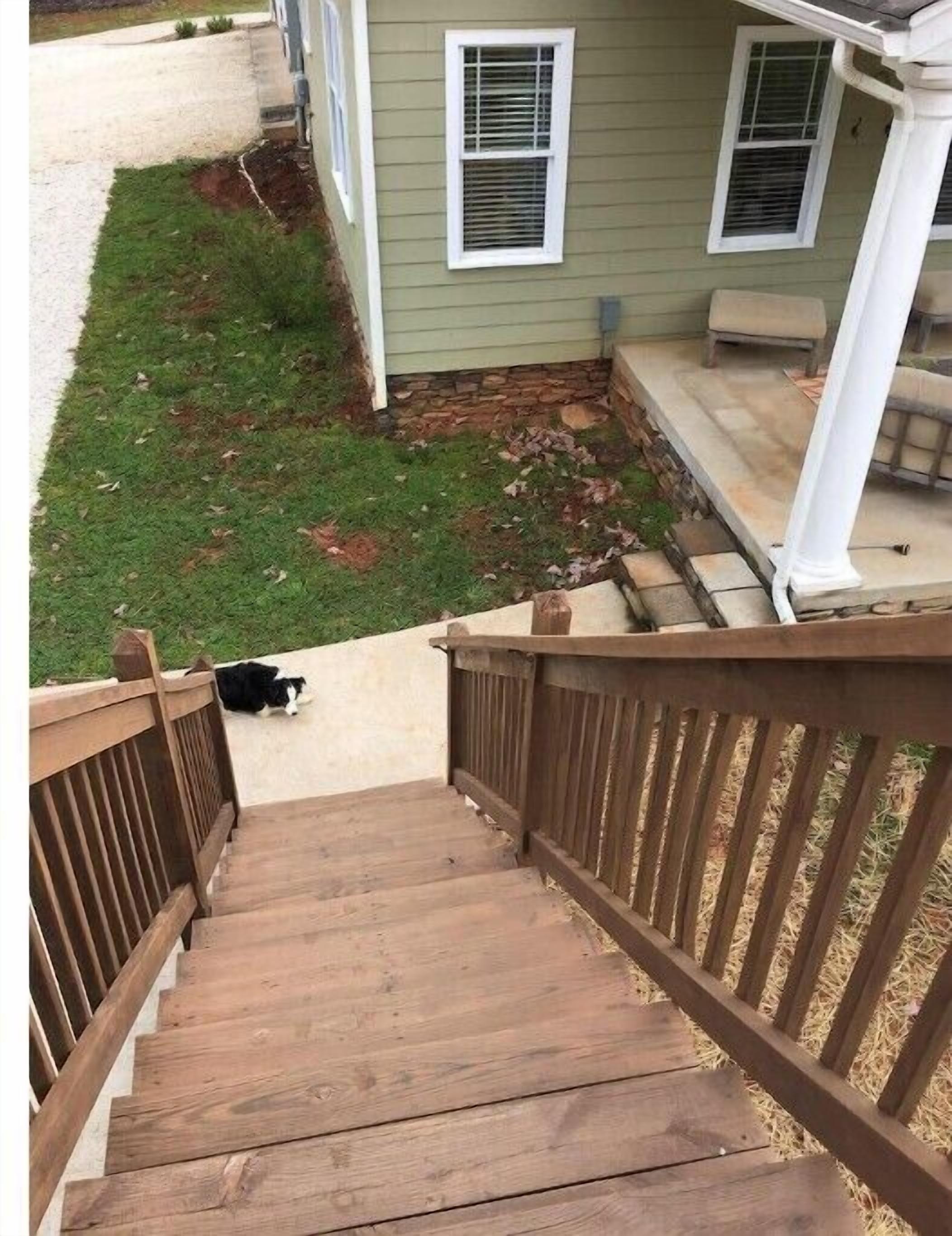 A wooden staircase leading to a porch with a stone foundation, a grassy yard, and a house with a chimney.