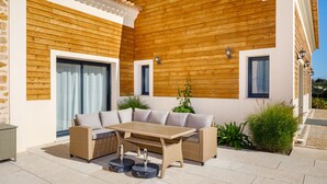 A patio with a wicker sofa, a wooden table, and potted plants. - LE VERGER ALGARVE VILLA (Estói)