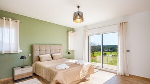 A bedroom with a large bed, a nightstand, a lamp, and a view of the outdoors through a sliding glass door. - LE VERGER ALGARVE VILLA (Estói)