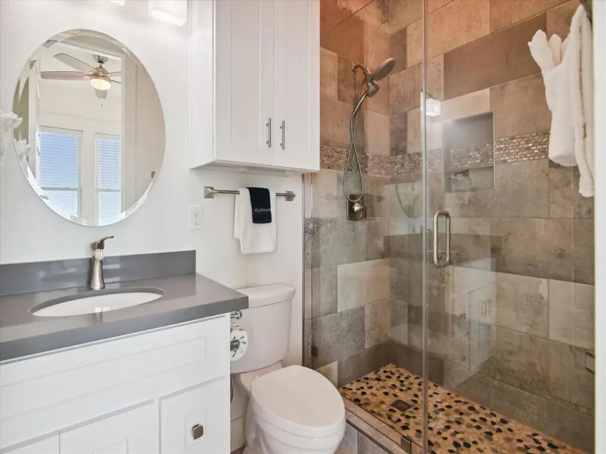 A modern bathroom with a glass-enclosed shower, a white sink, and a toilet.