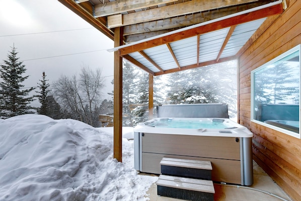 Une cabane en bois avec un jacuzzi et des marches menant à celui-ci, le tout entouré de neige.
