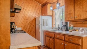 A kitchen with wooden cabinets, a white refrigerator, a stove, and a sink. - Pinetree Place (Wrightwood)