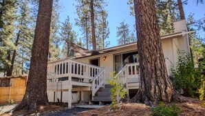 A cabin with a deck, surrounded by tall trees. - Pinetree Place (Wrightwood)