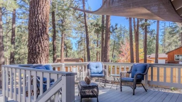 A wooden deck with outdoor seating, surrounded by tall trees. - Pinetree Place (Wrightwood)