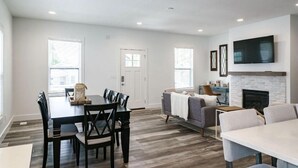Een moderne woonkamer met een open haard, een eethoek met een tafel en stoelen, en een bank.