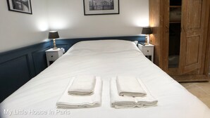 Una cama bien hecha con toallas blancas dobladas, un armario de madera y dos mesitas de noche con lámparas.