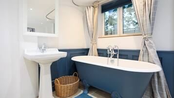 Ein Badezimmer mit einem weißen Waschtisch, einer freistehenden Badewanne und einem Fenster mit Vorhängen.