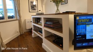 Una habitación acogedora con una estantería de madera, un televisor de pantalla plana y un ventanal con cortinas.