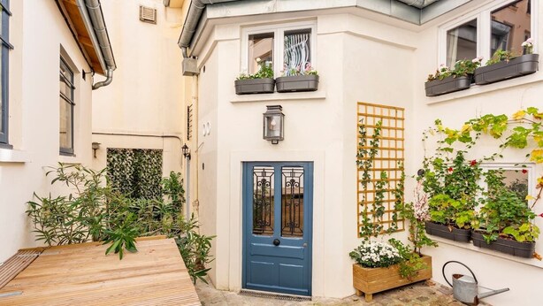 Un patio con una puerta azul, plantas en macetas y una terraza de madera.