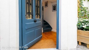 Una puerta azul con un panel de vidrio y un picaporte de metal, que da acceso a una escalera con barandilla de madera.