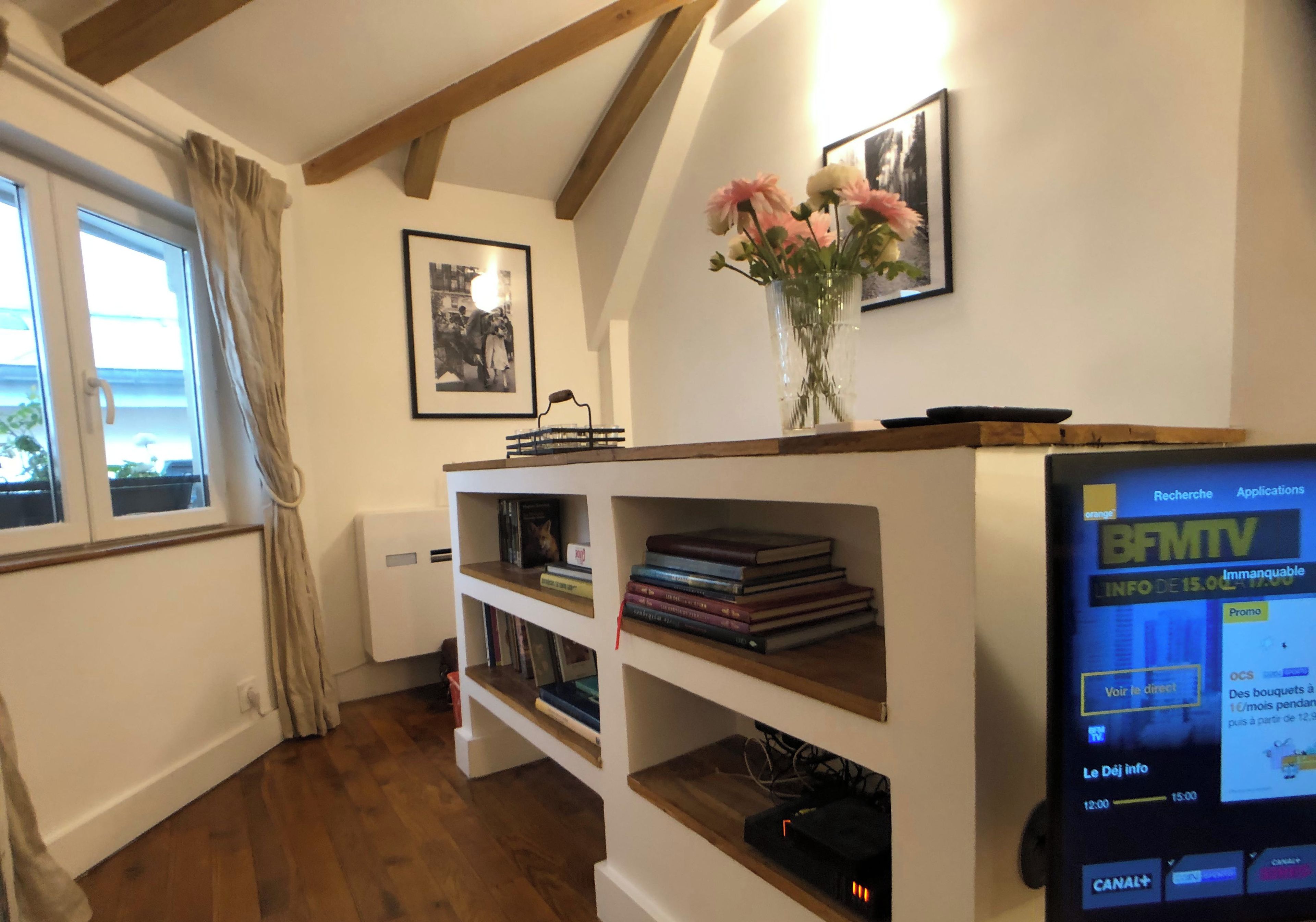 Une pièce chaleureuse avec une bibliothèque en bois, un téléviseur à écran plat et une fenêtre avec des rideaux.