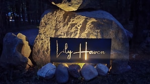 Una señal con el nombre 'Lily Haven' en cursiva sobre un fondo oscuro, rodeada de rocas y un gran bloque de piedra.