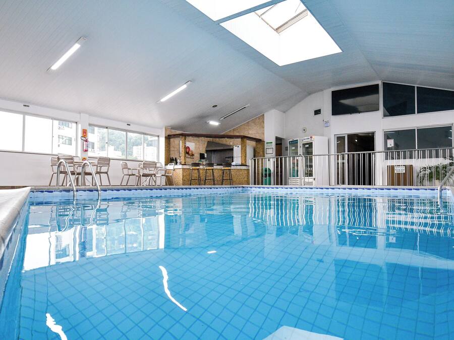 Una piscina interior con agua azul cristalina, un área de bar y un espacio de descanso con sillas.