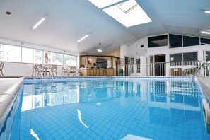 An indoor swimming pool with clear blue water, a bar area, and a seating area with chairs. - HOTEL JARAGUA (Joacaba)