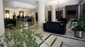 Eine Hotelhalle mit Empfangsbereich, Sitzgelegenheiten und einer großen Pflanze.