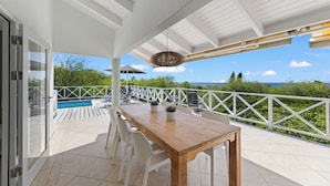 Un espace extérieur abrité, doté d’une table et de chaises en bois, d’une rambarde blanche et offrant une vue sur la mer.