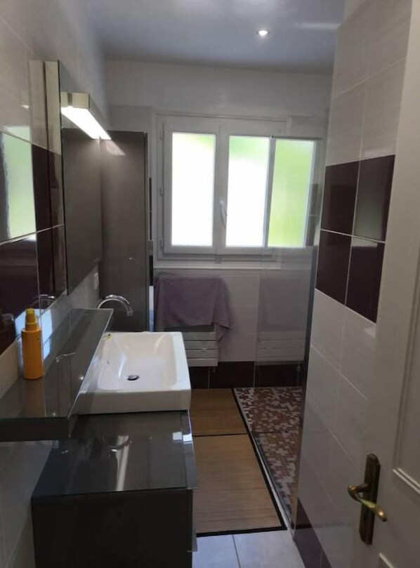 Un baño pequeño con un lavabo blanco, un espejo y una ventana sobre el lavabo.