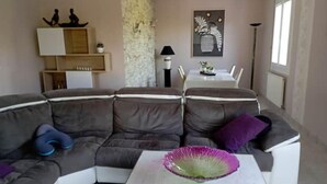 A modern living room with a sectional sofa, a coffee table, a dining table with chairs, and a wall-mounted shelf with decorative items. - Beautifull house with swimmingpool in Dordogne (Allemans)