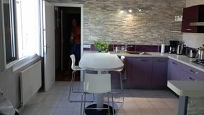 A modern kitchen with a stone backsplash, a dining table with chairs, and a person in the doorway. - Beautifull house with swimmingpool in Dordogne (Allemans)