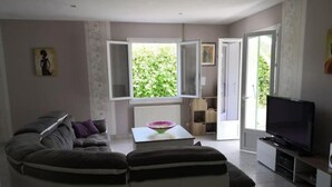 A living room with a sofa, a coffee table, a TV, and a window with a view of greenery. - Beautifull house with swimmingpool in Dordogne (Allemans)