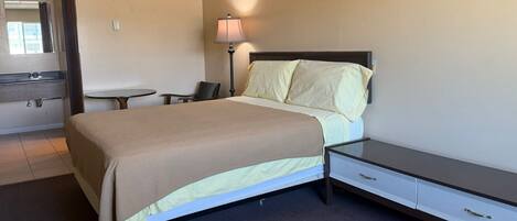 Una habitación de hotel con cama, mesita de noche, lámpara, silla y una pequeña mesa.