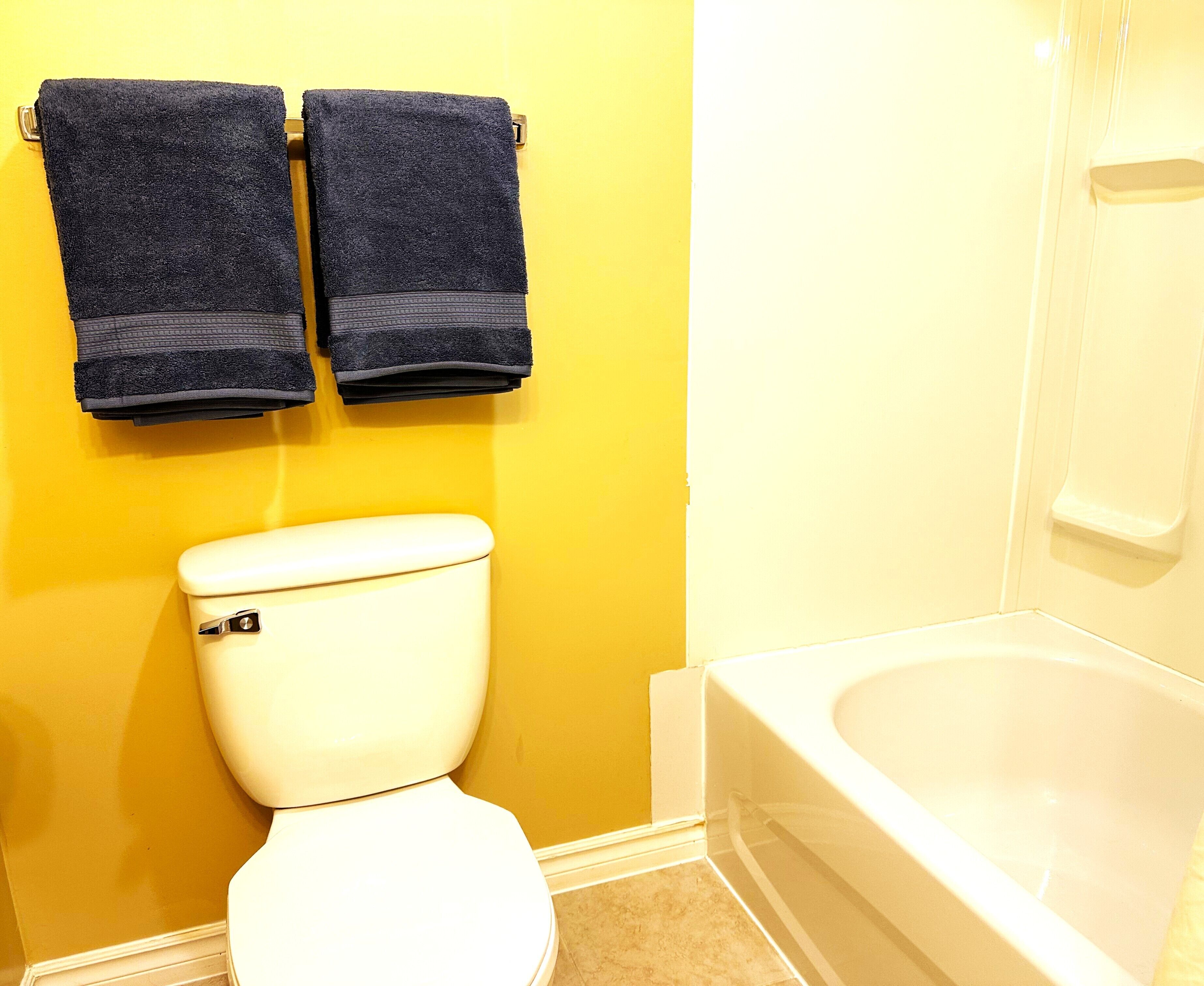 A bathroom with a white toilet, yellow walls, and a bathtub.