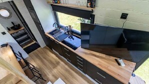 A compact kitchen with a wooden countertop, dark cabinets, and a window providing a view of the outdoors.