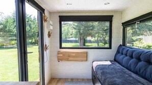 A cozy room with a large window, a cushioned bench, and a wooden shelf.