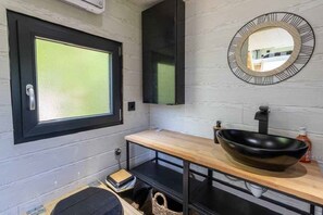 Un baño moderno con un amplio ventanal, un lavabo negro y un espejo redondo en la pared.