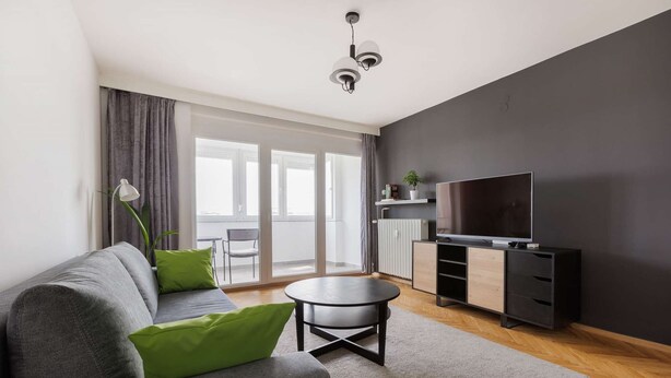 A modern living room with a grey sofa, a small round table, and a TV on a black stand.
