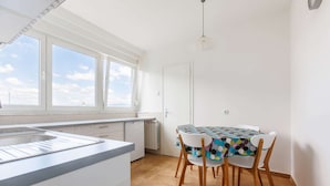 A bright kitchen with a large window, a dining table with colorful chairs, and a white door.
