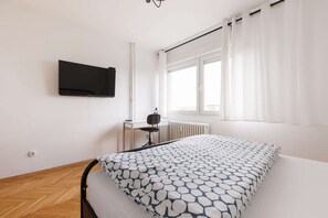 Et soveværelse med seng, et fjernsyn monteret på væggen, en radiator og et vindue med gardiner.