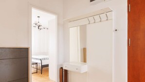 A hallway with a wooden floor, a white wall, and a mirror above a white cabinet.