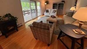 A living room with a sofa, armchair, and coffee table, a sliding glass door leading to a balcony, and a small side table with a lamp. - Hidden oasis with northern feel (Cloquet)