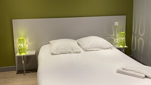 Siististi pedattu sänky valkoisilla lakanoiden kanssa, kaksi yöpöytävalaisinta, joissa on vihreät varjostimet, ja moderni sängynpääty.