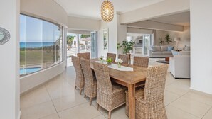 A spacious dining area with a large table and wicker chairs, overlooking a scenic view of the ocean.