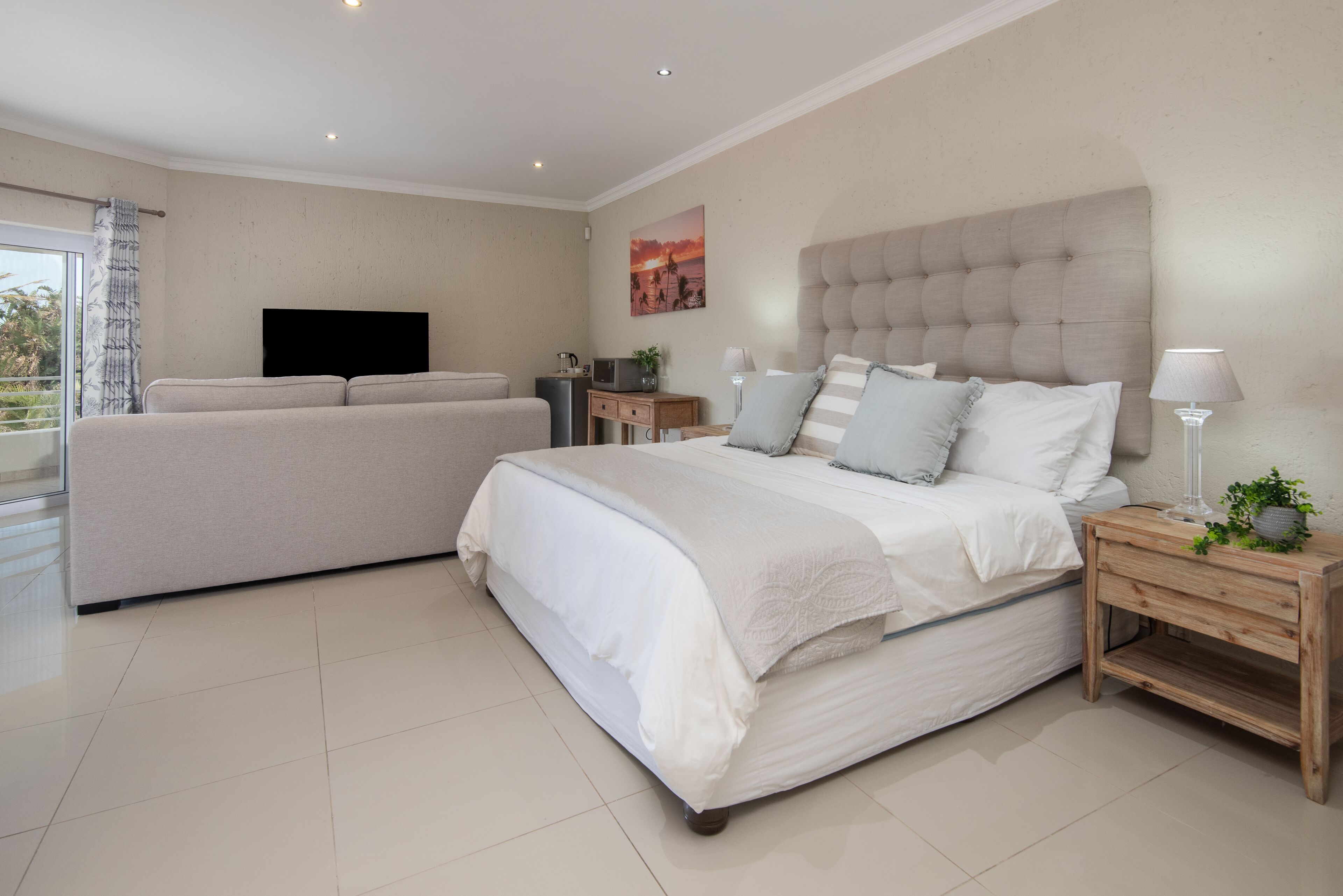 A bedroom with a large bed, a sofa, a television, and a small table with a lamp.