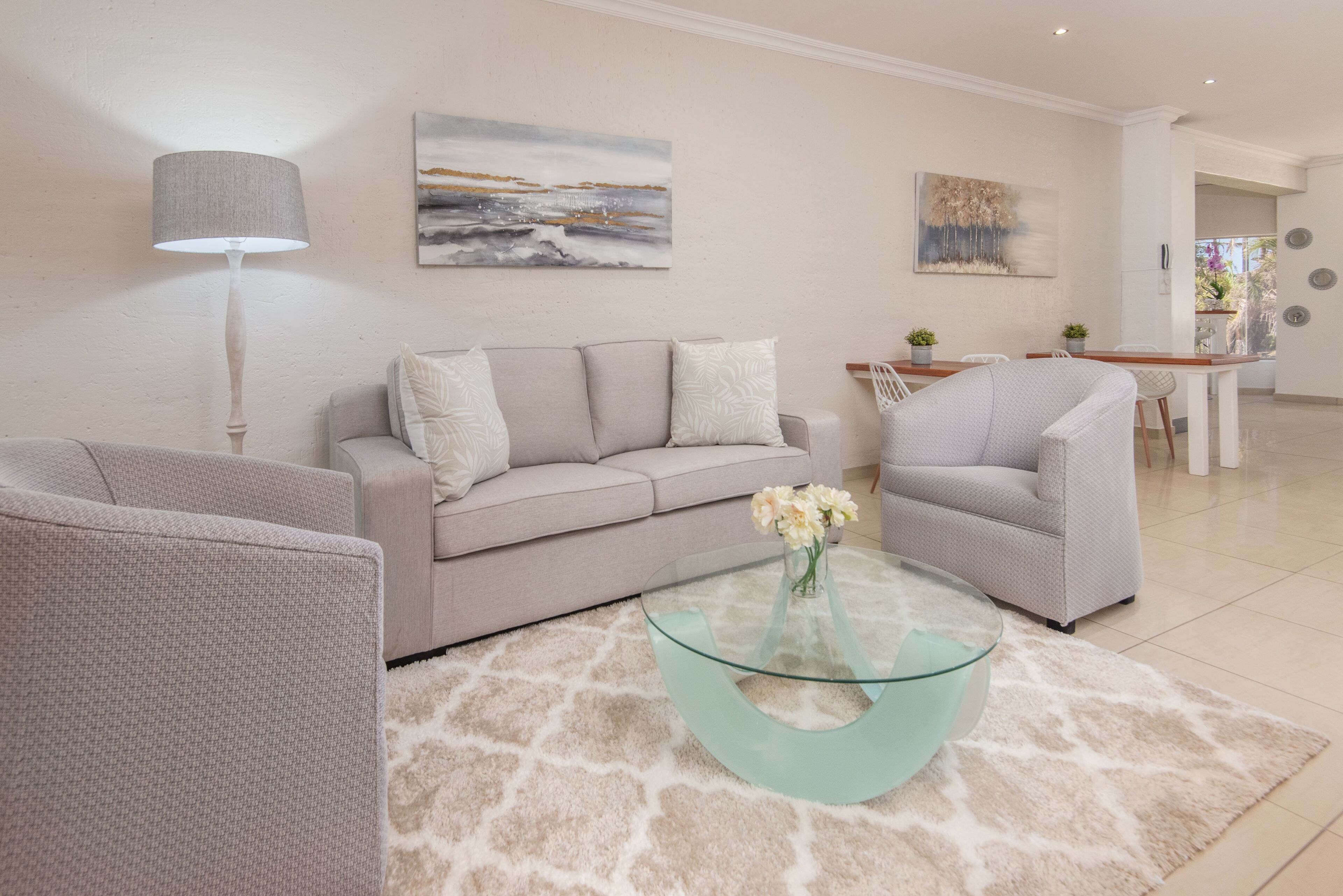 Una sala de estar moderna con sofá, sillones, una mesa de centro de vidrio y una lámpara.