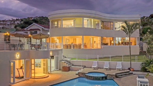 Una casa moderna de dos pisos con piscina, mobiliario exterior y una escalera que lleva al piso superior.