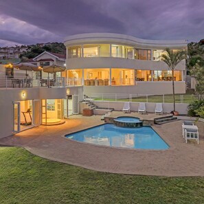 Una casa moderna de dos pisos con piscina, mobiliario exterior y una escalera que lleva al piso superior.
