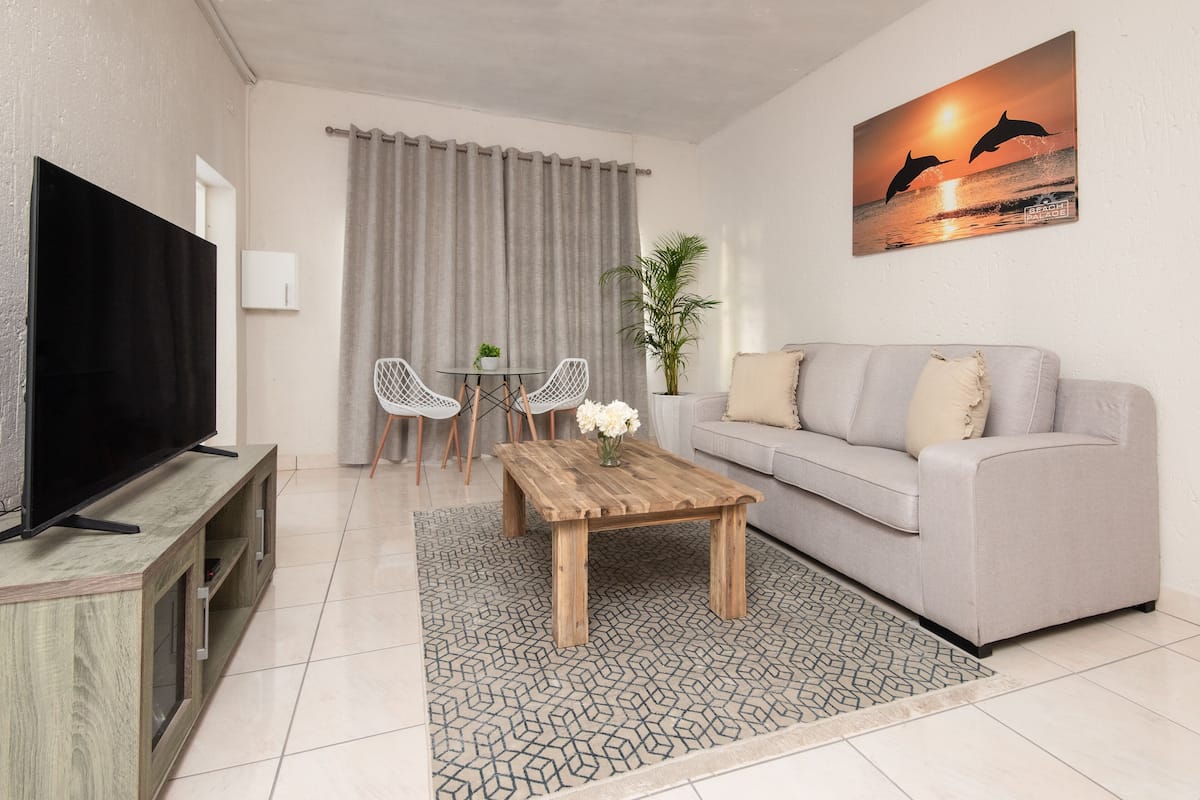 Uma sala de estar com televisão de tela plana, mesa de centro de madeira, sofá cinza e um quadro de golfinhos.