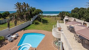 A rooftop pool with a view of the ocean, surrounded by palm trees and a patio area with outdoor seating.
