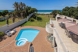 A rooftop pool with a view of the ocean, surrounded by palm trees and a patio area with outdoor seating.