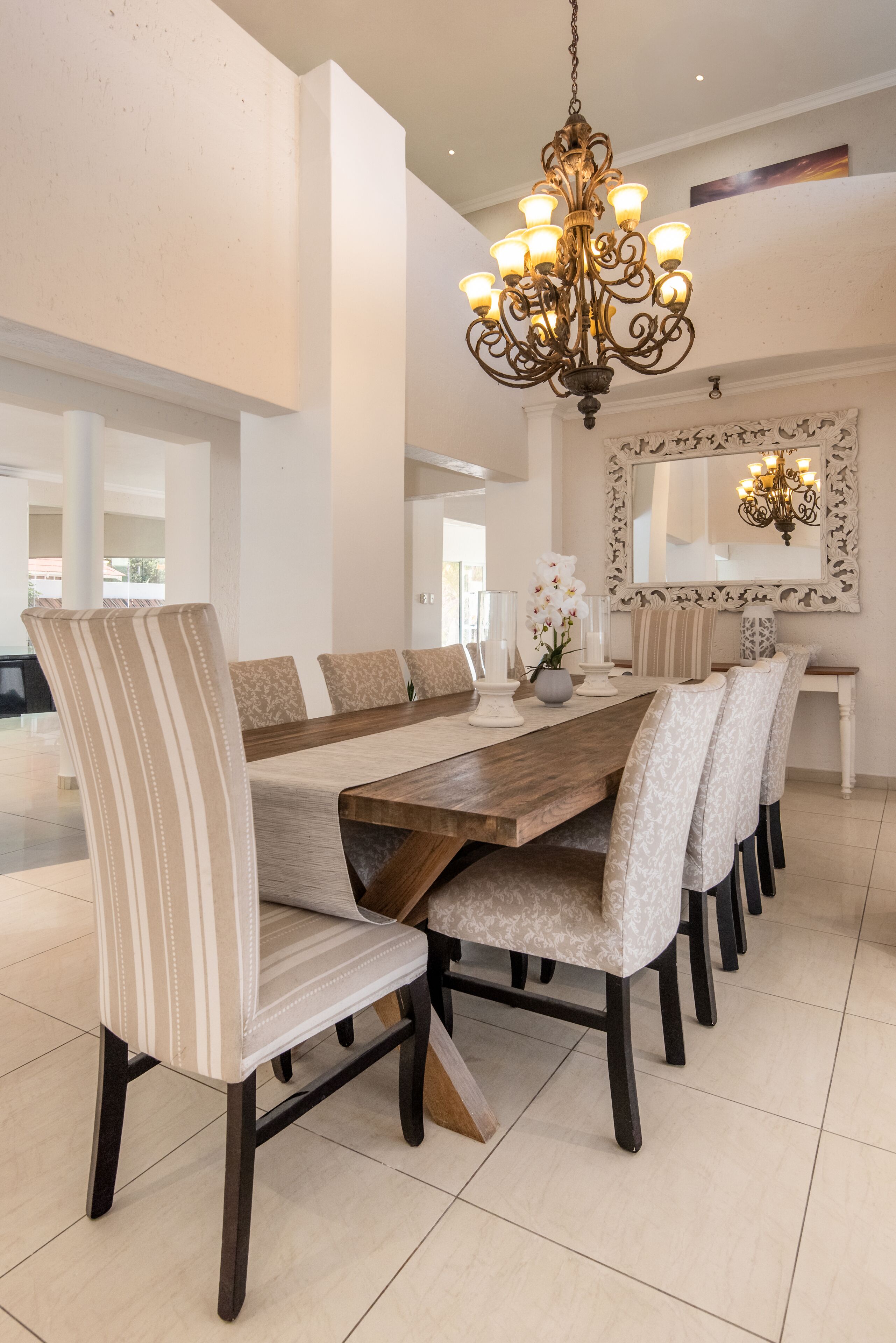 A dining area with a long wooden table, striped chairs, and a chandelier.
