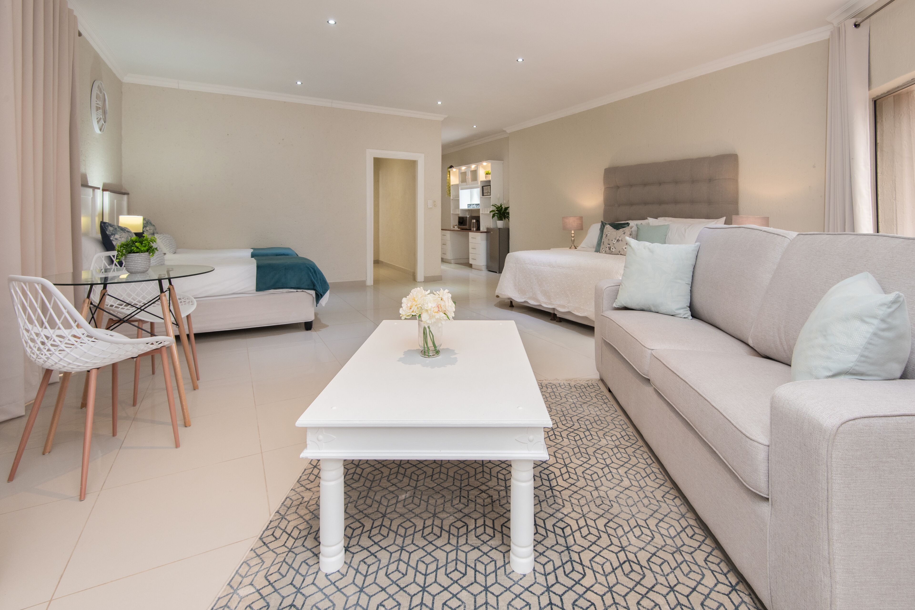 Una sala de estar moderna con un sofá blanco, una mesita de centro blanca y una zona de comedor con una mesa de cristal y sillas blancas.