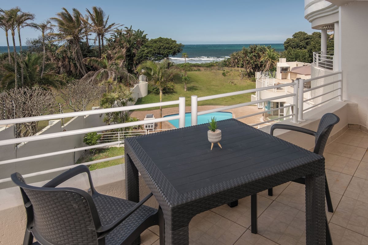 Varanda com mesa e cadeiras, com vista para uma piscina e o oceano.