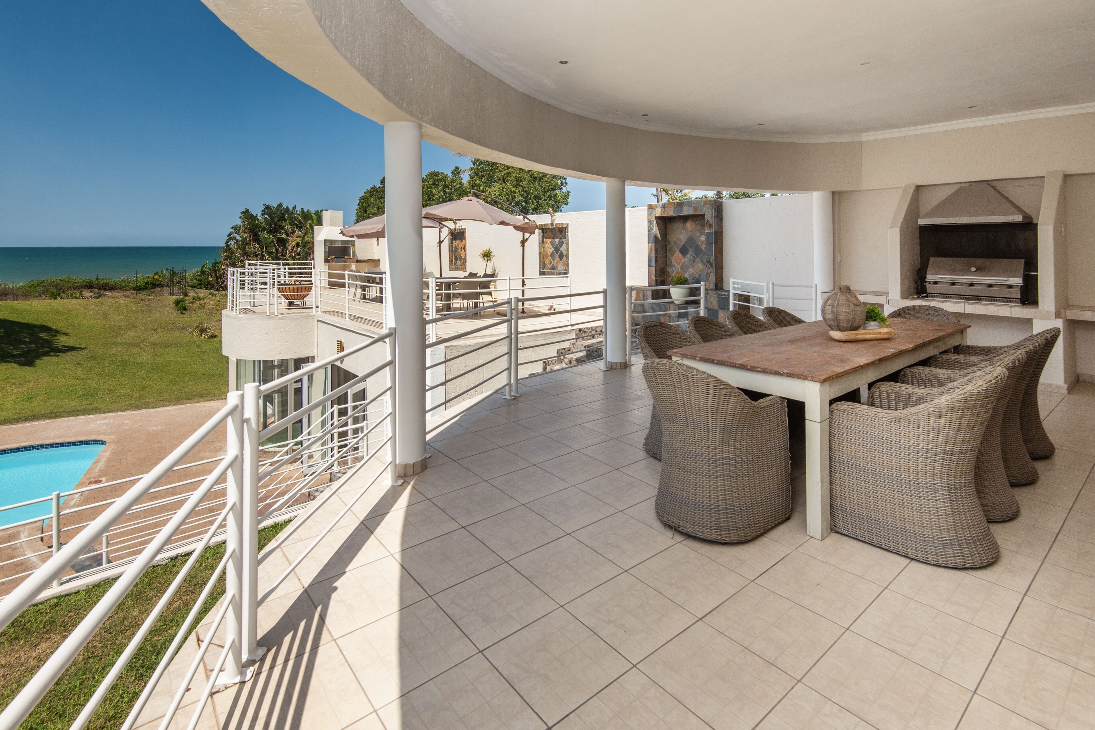 Un patio techado al aire libre con mesa y sillas, una parrilla y una piscina.