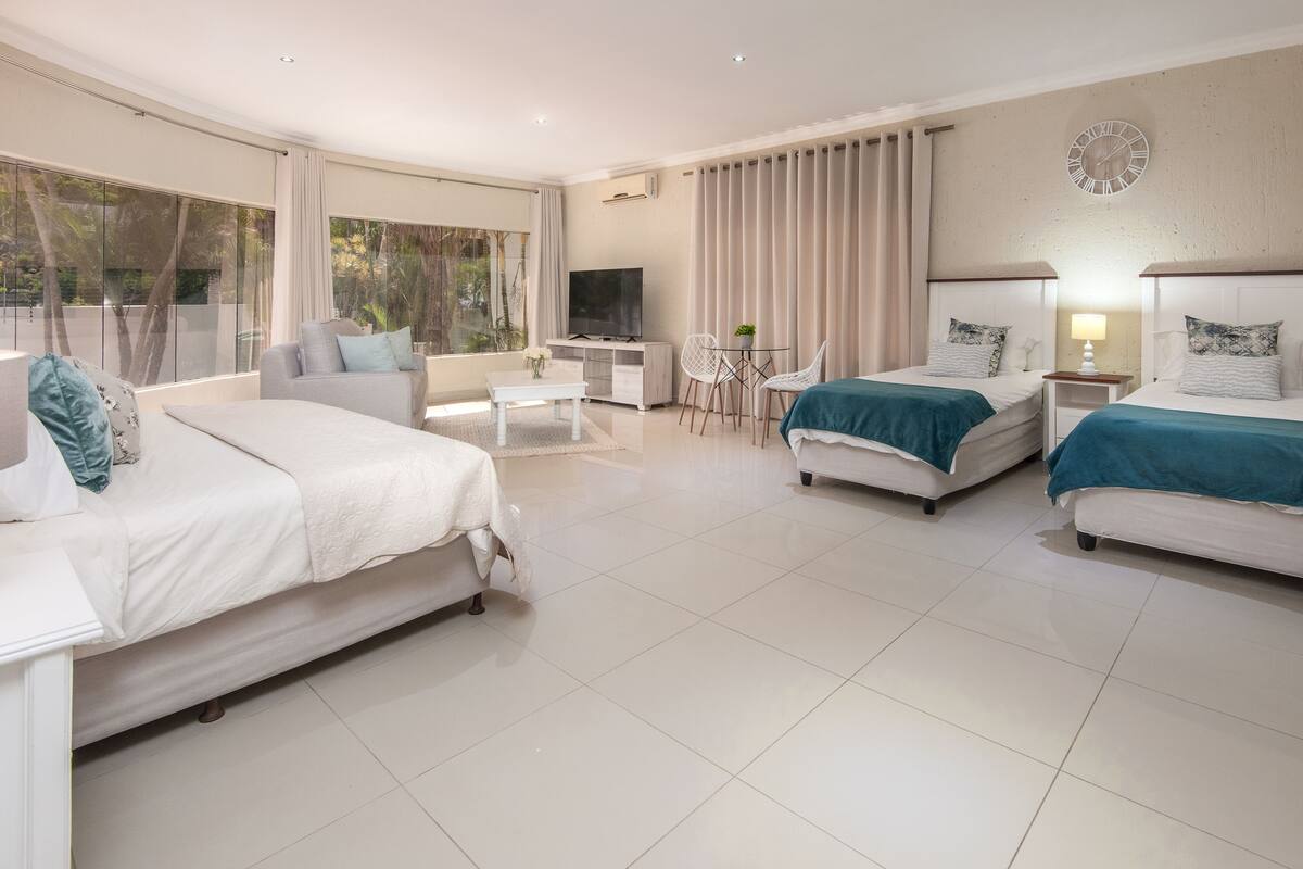 Quarto de hotel moderno com duas camas, um sofá, uma televisão e uma área de refeições.