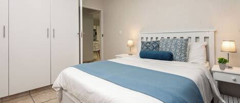 A bedroom with a bed, white wardrobe, bedside tables with lamps, and a door leading to another room.