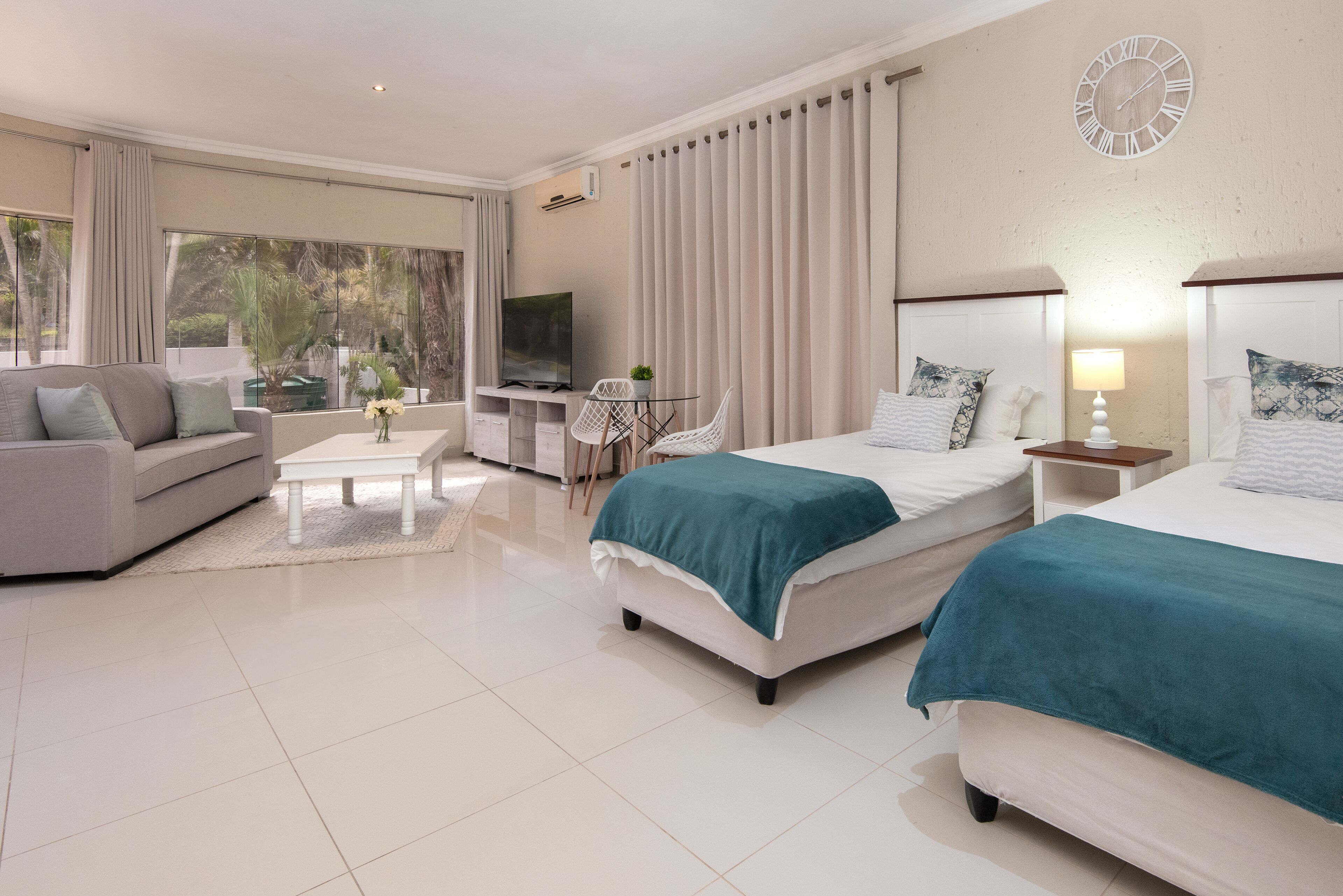 A modern hotel room with two beds, a sofa, a TV, and a dining area.